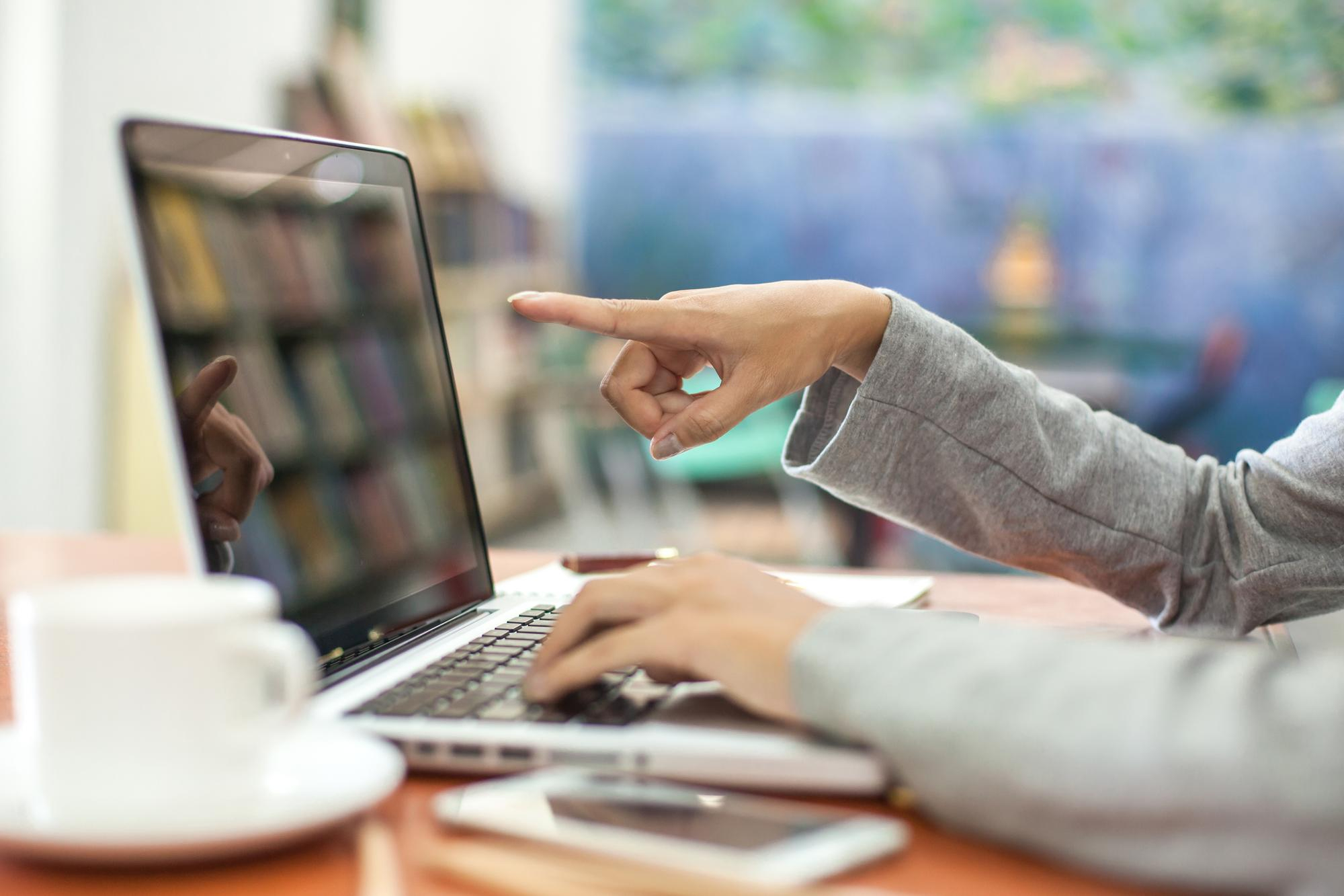 Persona señalando la pantalla de un portátil mientras trabaja en una oficina o biblioteca