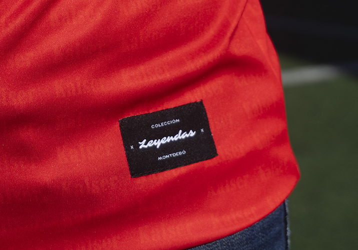 Etiqueta de la colección Leyendas | Montdebó Fotografía de detalle de la etiqueta «Colección Leyendas Montdebó» sobre una camiseta deportiva roja.