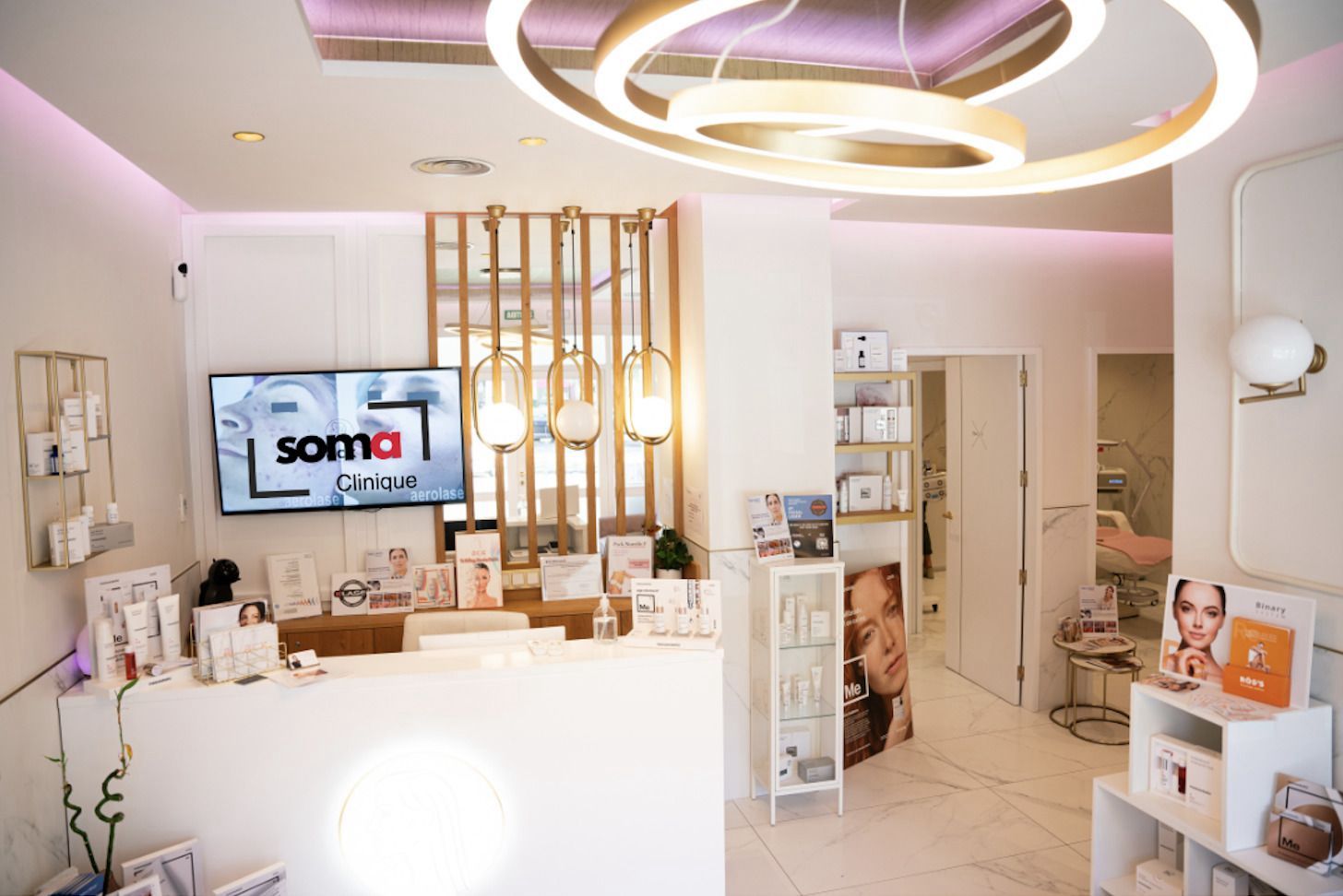 Instalaciones de clínica de medicina estética | Lum Clinic Interior de la recepción de una clínica de medicina estética, con mostrador blanco, iluminación decorativa, expositores de productos y zona de tratamientos al fondo.
